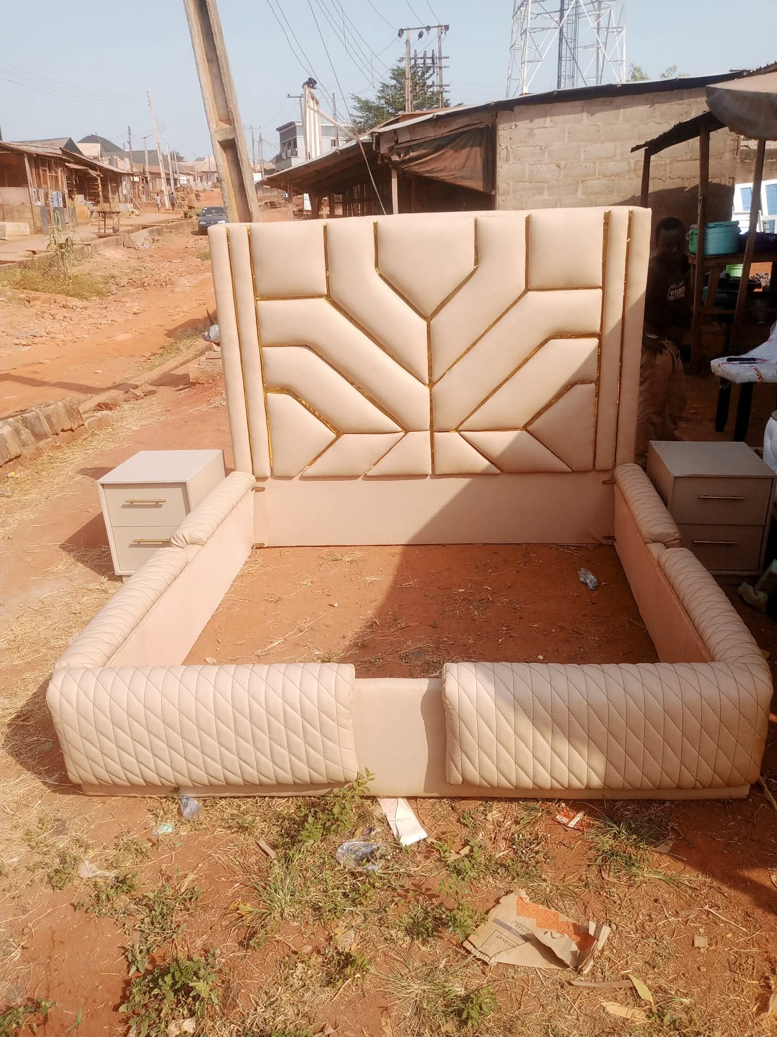 Completed light cream custom bedframe with geometric upholstered headboard, quilted rails and matching bedside cabinets at the workshop
